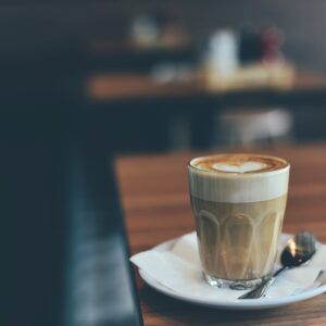 clear drinking glass with brown beverage in white saucer in tilt shift photography