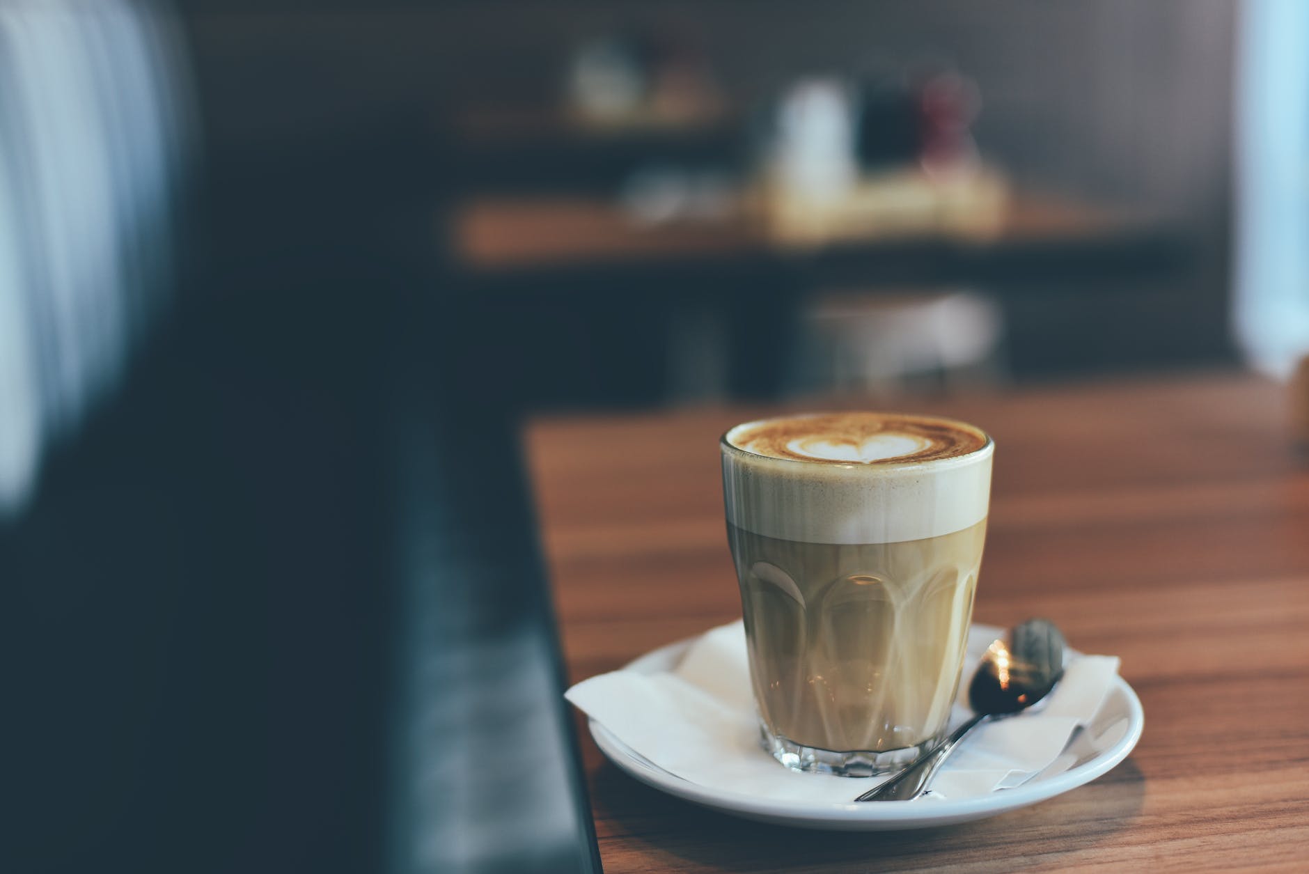 clear drinking glass with brown beverage in white saucer in tilt shift photography