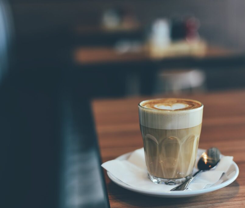 clear drinking glass with brown beverage in white saucer in tilt shift photography